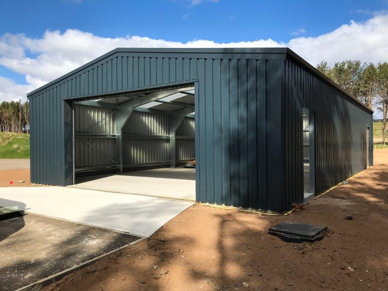 Large slate blue steel building under construction with an open front bay and side entrance.